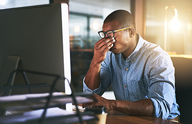 Man pinching his eyes with his hand while sitting in front of a computer.